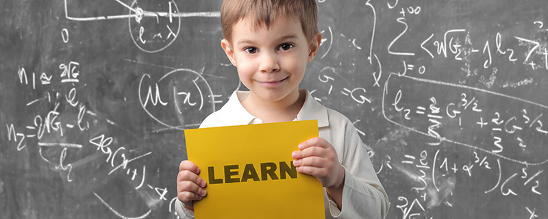 Young boy holding learn sign in front of a blackboard