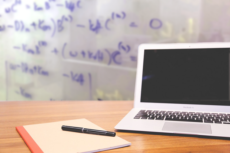Laptop on a desk with a notebook and pen in front of it. 