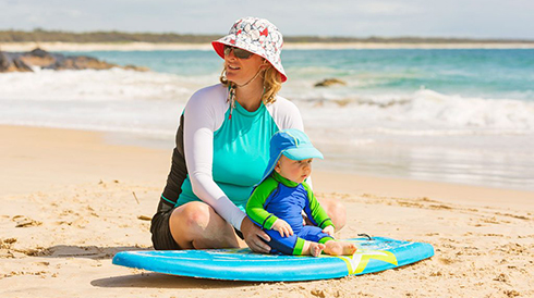Mom sitting with baby on a surfboard at the beach