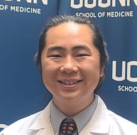Man wearing dress shirt, tie, and lab coat smiling at camera