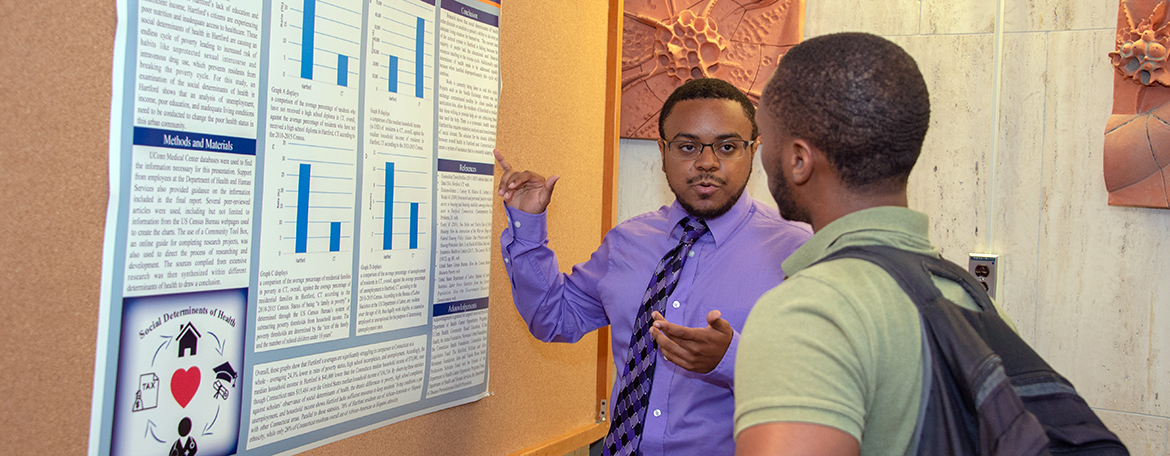 Student in the Summer Research Fellowship Program presenting his poster presentation to another student