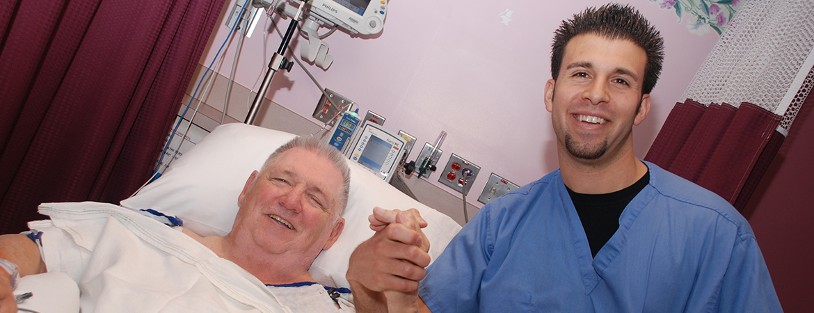 Male nurse in blue scrubs holding the hand of a male patient