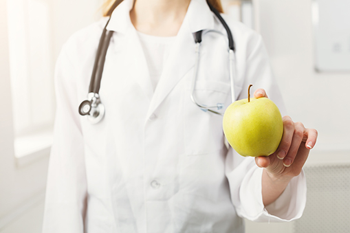 Unrecognizable nutritionist woman with green apple sitting at office
