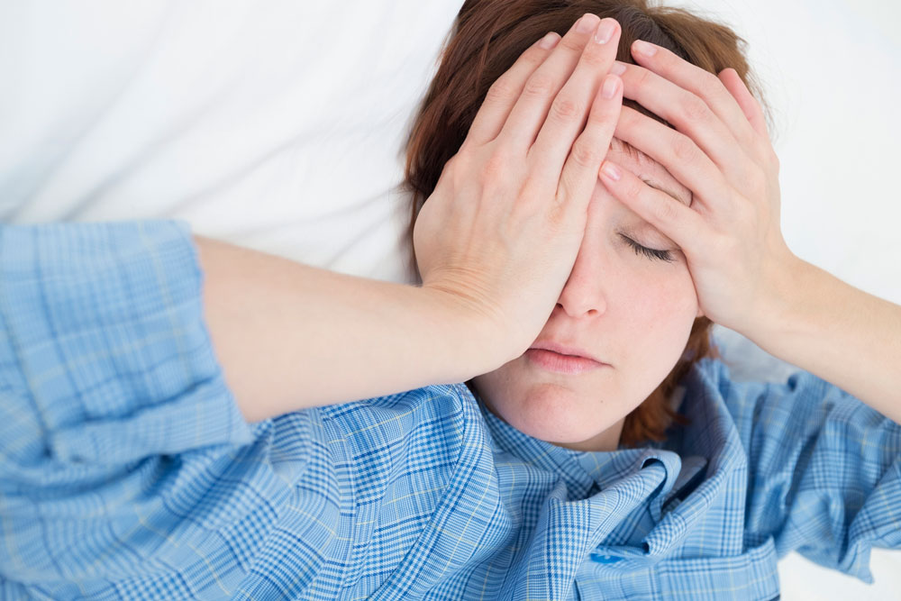 Mid adult woman wearing pajamas lying down with hands covering face.