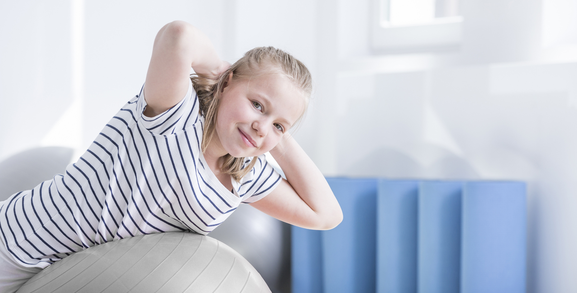Child smiling at camera laying on ball during physical therapy session