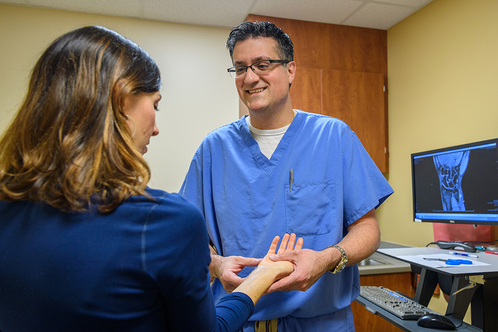 Dr. Joel Ferreira examining a female patient's hand and wrist