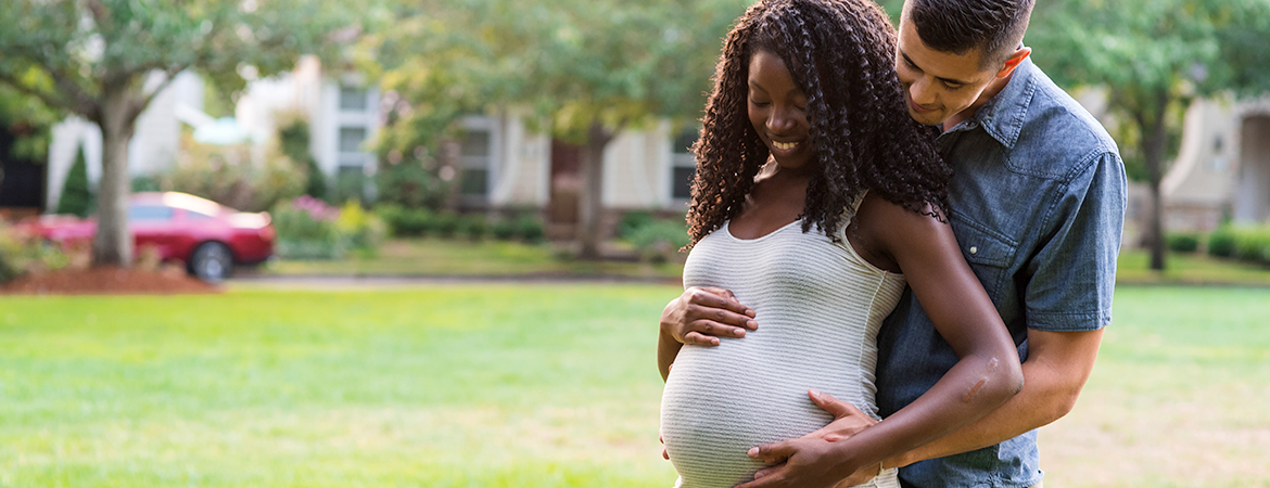 Interracial pregnant couple pose in a city park on a beautiful day