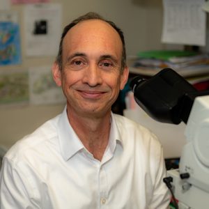 Enrique Ballesteros, M.D., sitting next to a microscope