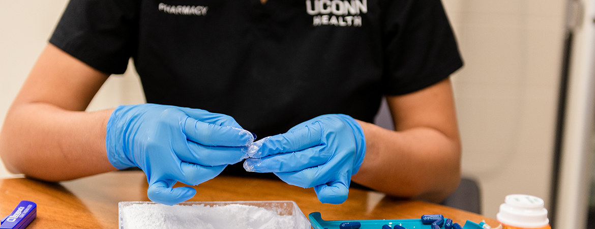 A pair of gloved hands fills capsules in the pharmacy at UConn Health