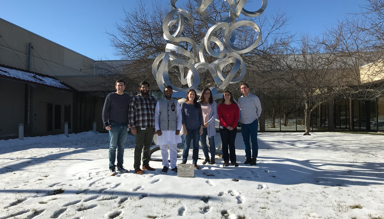 A group photo of the lab, outdoors in front of a sculpture. From right to left: Rotation student Nicholas Jannetty, Prakhar Bansal, Yuva Kondaveeti, Heather Glatt-Deeley, Erin Banda, Darcy Ahern, and Stefan Pinter.