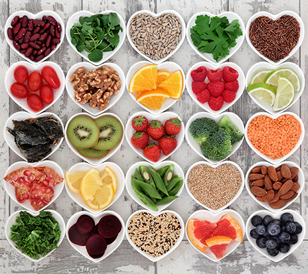 A variety of healthy food choices (fruits, vegetables, nuts, grains) in heart shaped cups arranged 5 by 5 on a weathered wooden floor