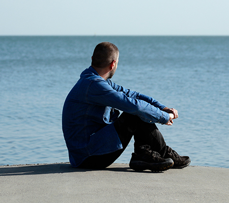 Man sitting on a beach staring out to sea