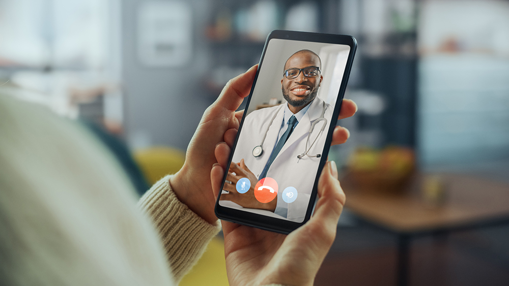 Woman's hands holding cell phone with video of doctor on a telehealth call.