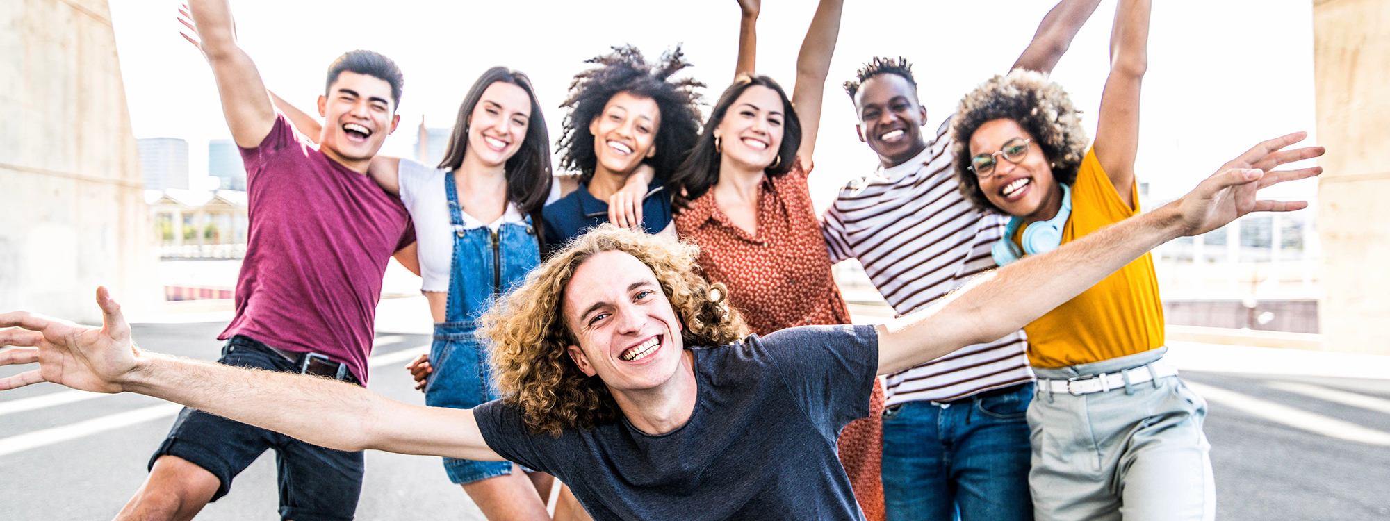 Big group of happy friends stands on city street with raised arms together