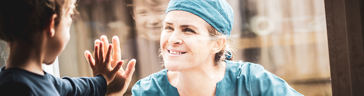 Mature healthcare worker posing seeing her son with a window glass separating them to avoid possible contagion