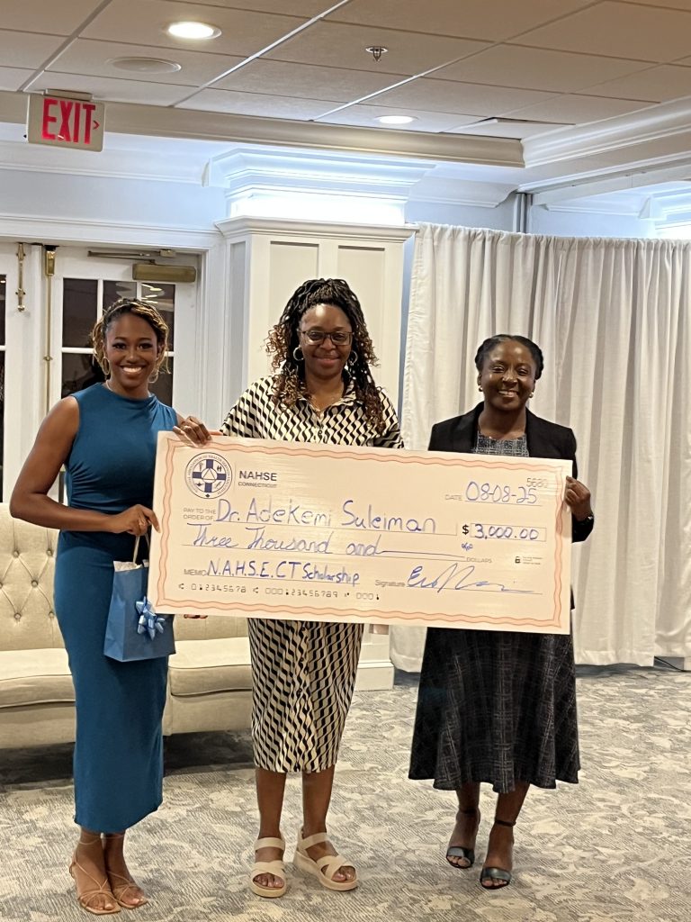 PhD Student, Adekemi Suleiman stands amongst two women holding a large check that rreads three thousand dollars for the N.A.H.S.E CT Scholarship