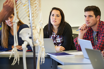Medical students sitting in an anatomy class looking at a skeleton