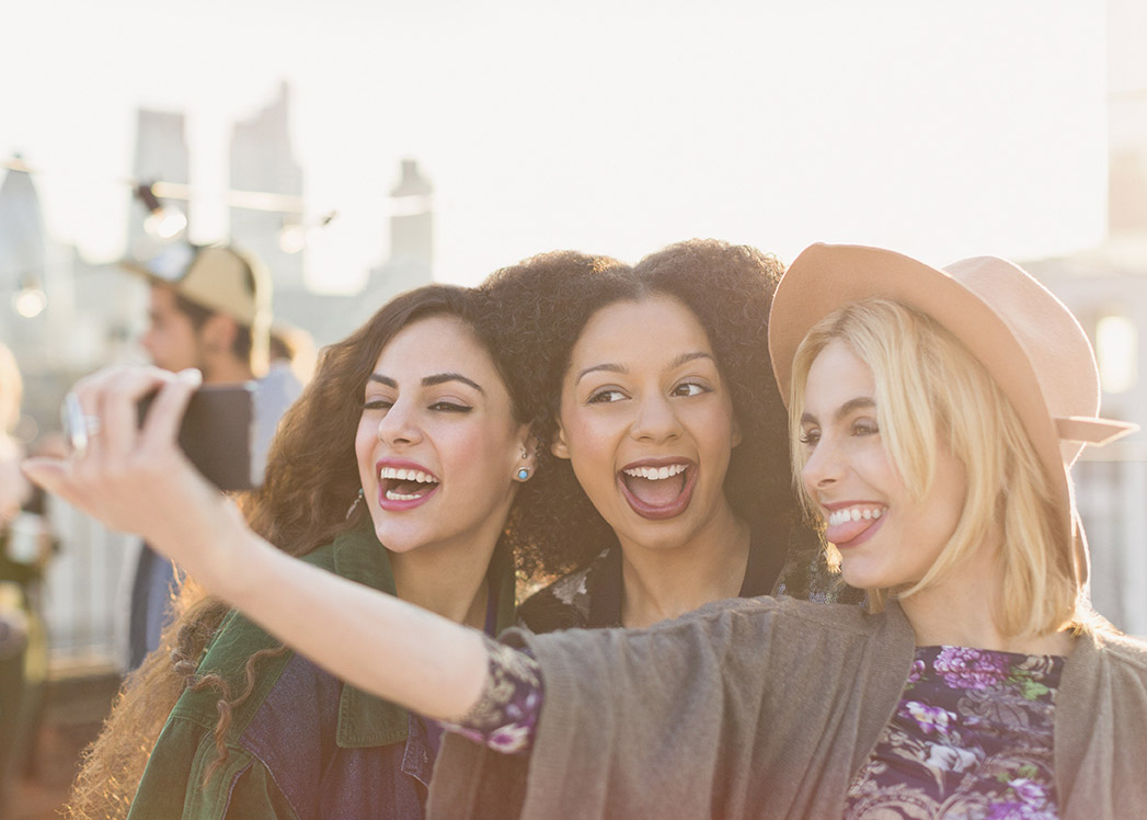 Enthusiastic young women taking selfie at rooftop party.