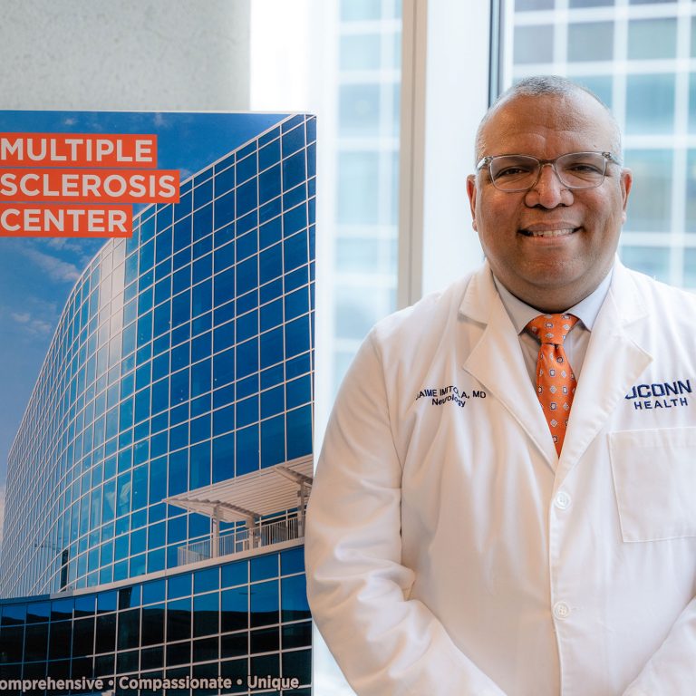 Dr. Jaime Imitola portrait white coat next to Multiple Sclerosis Center sign